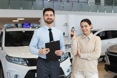 Happy salesman and client with key near new car in salon