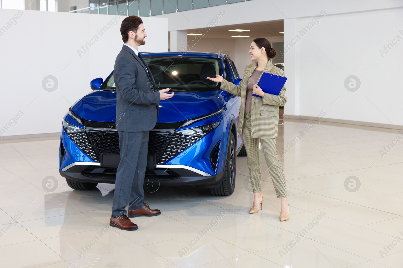 Photo of Happy saleswoman and client near new blue car in salon