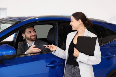 Photo of Happy saleswoman giving key to client inside new car in salon