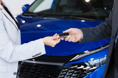 Salesman giving key to client near new car in salon, closeup