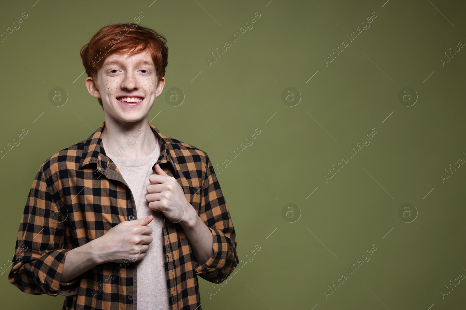 Photo of Portrait of smiling teenage boy with freckles on dark green background. Space for text