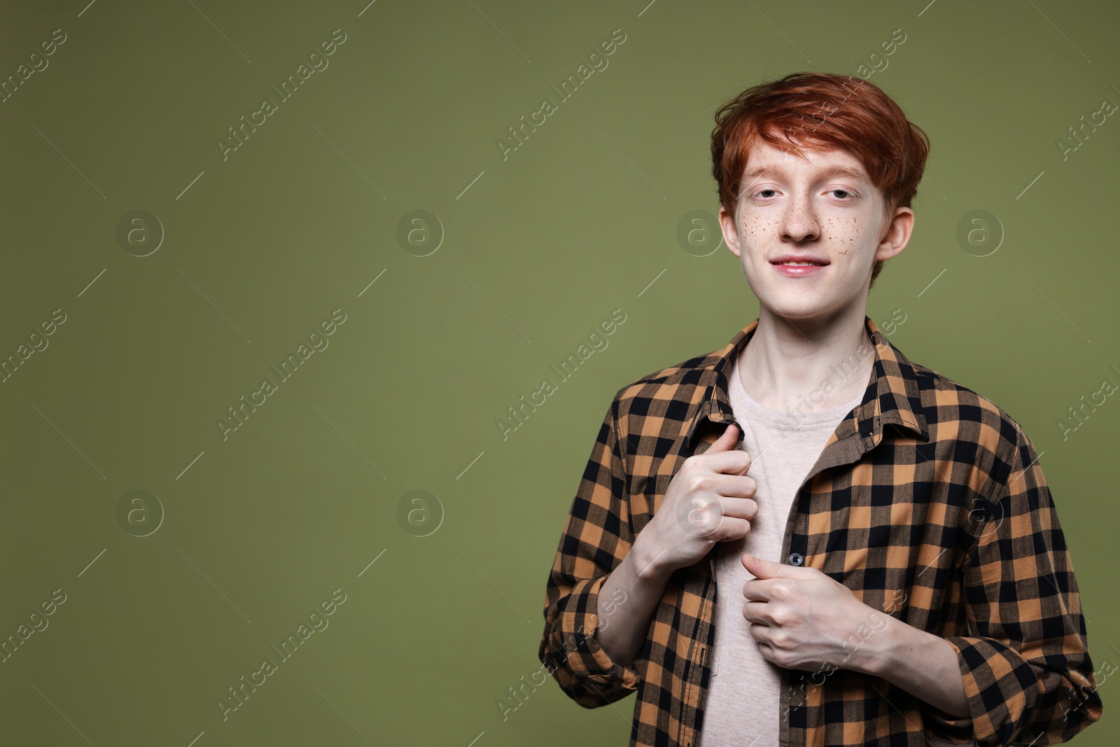 Photo of Portrait of smiling teenage boy with freckles on dark green background. Space for text