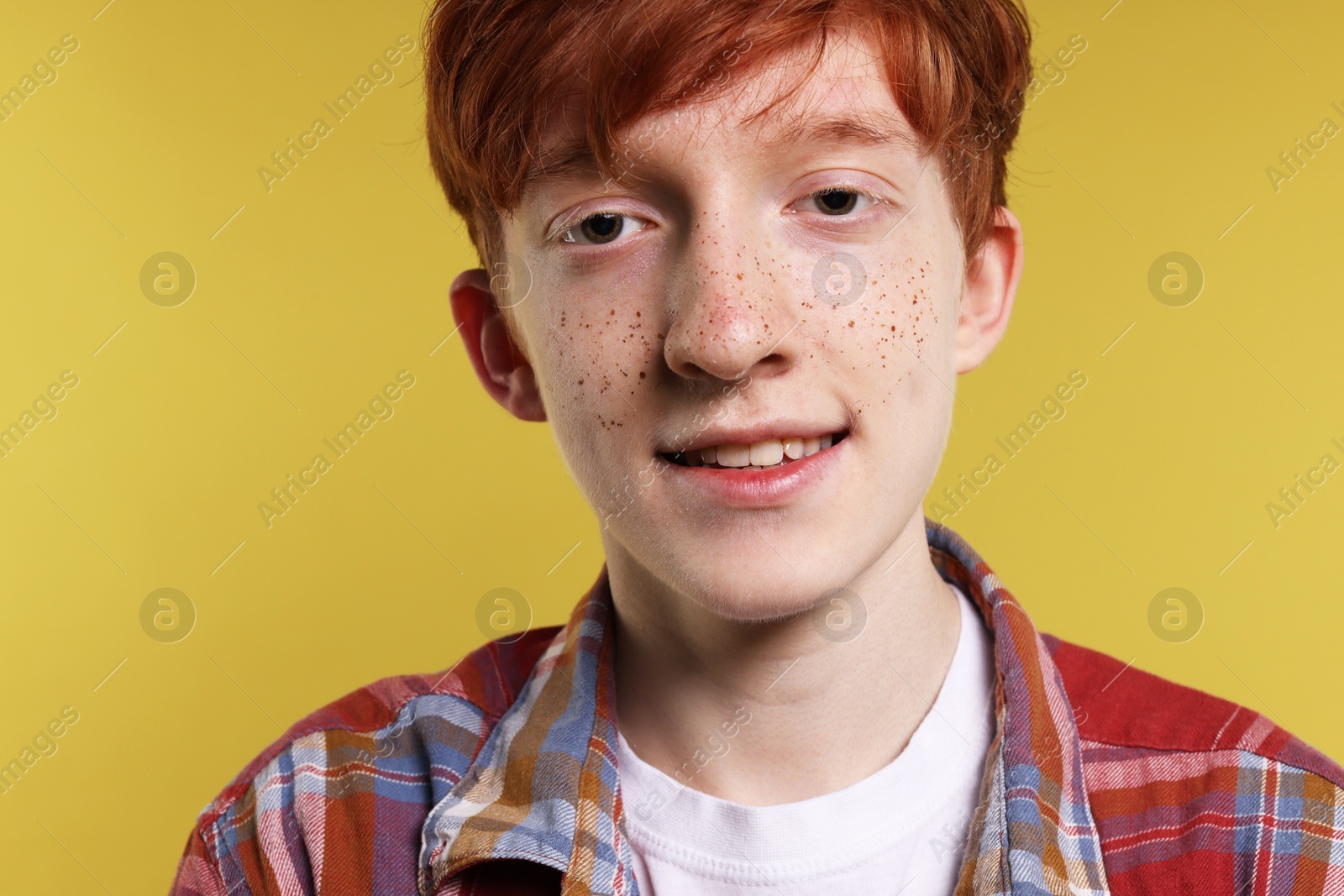 Photo of Smiling teenage boy with freckles on yellow background, closeup