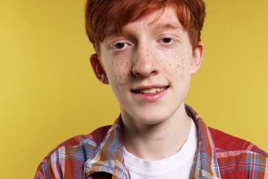 Photo of Smiling teenage boy with freckles on yellow background, closeup