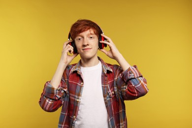 Photo of Cute teenage boy with freckles listening to music by headphones on yellow background