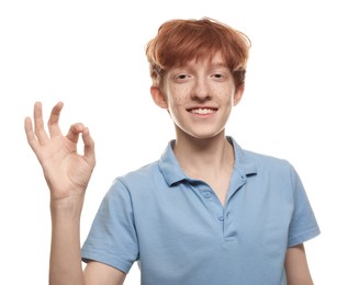 Photo of Smiling teenage boy with freckles showing ok gesture on white background