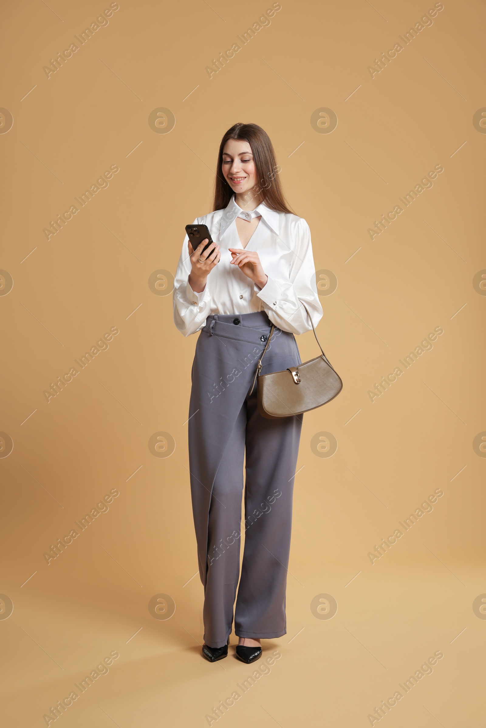 Photo of Beautiful woman in stylish outfit with smartphone on beige background