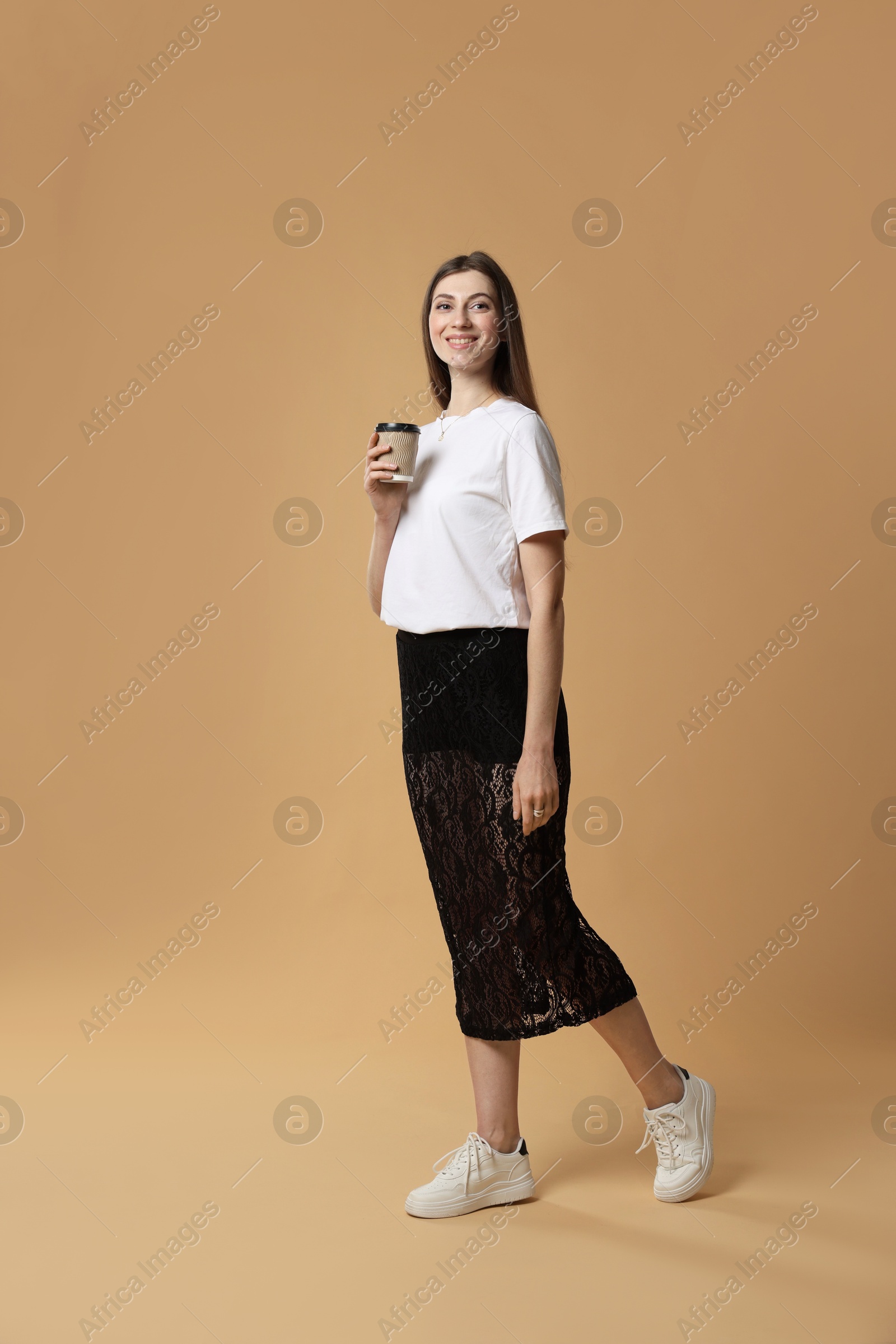 Photo of Beautiful woman in stylish outfit with cup of coffee on beige background