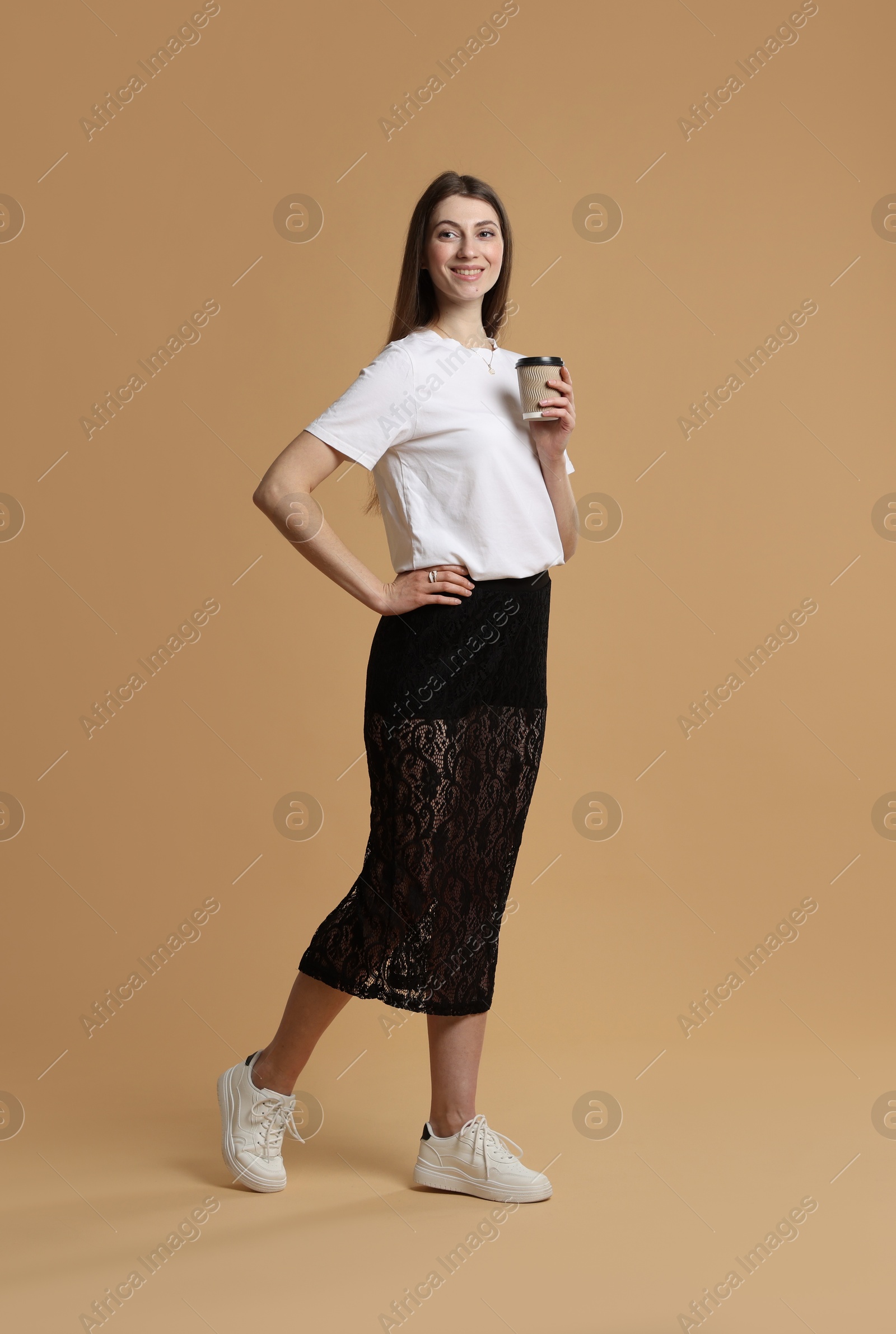 Photo of Beautiful woman in stylish outfit with cup of coffee on beige background