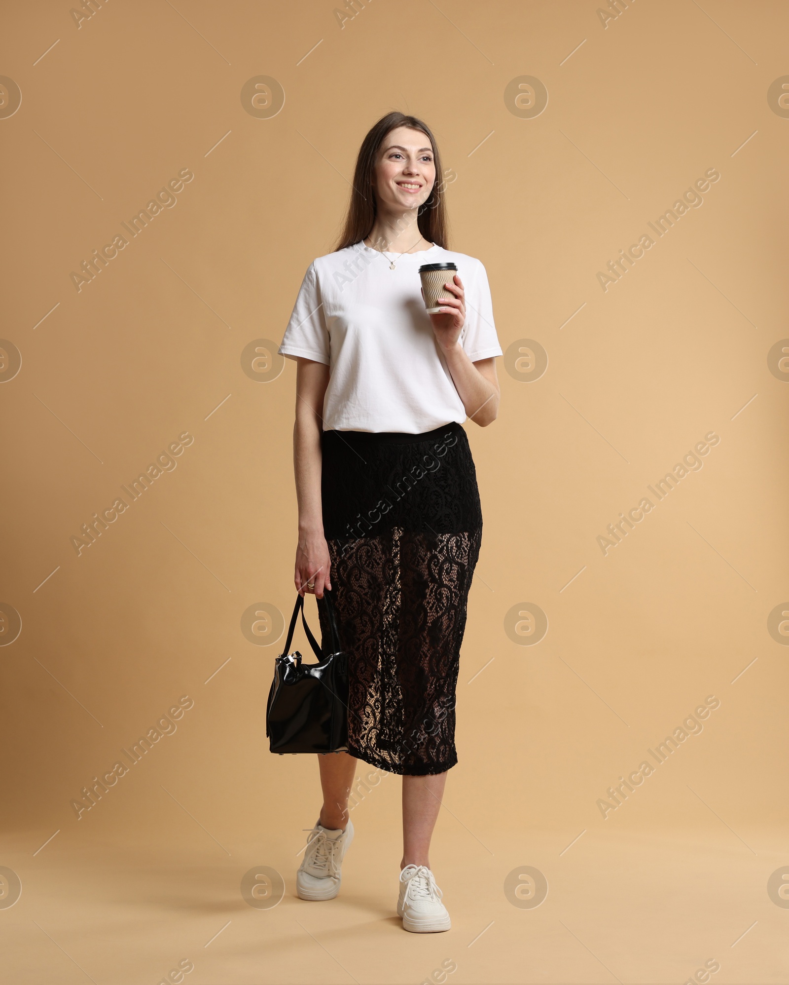 Photo of Beautiful woman in stylish outfit with cup of coffee on beige background