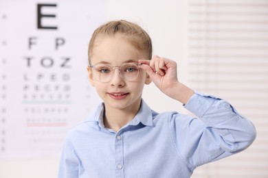 Photo of Little girl wearing glasses near vision test chart at ophthalmologist office