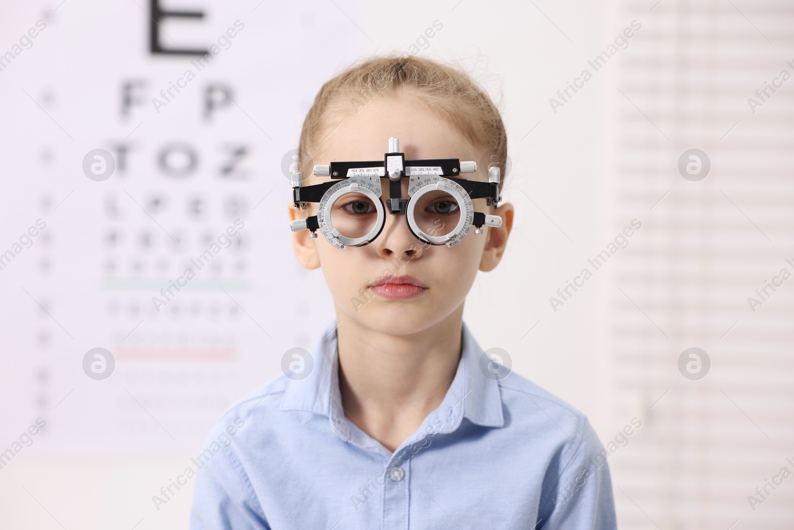 Photo of Little girl with trial frame near vision test chart at ophthalmologist office