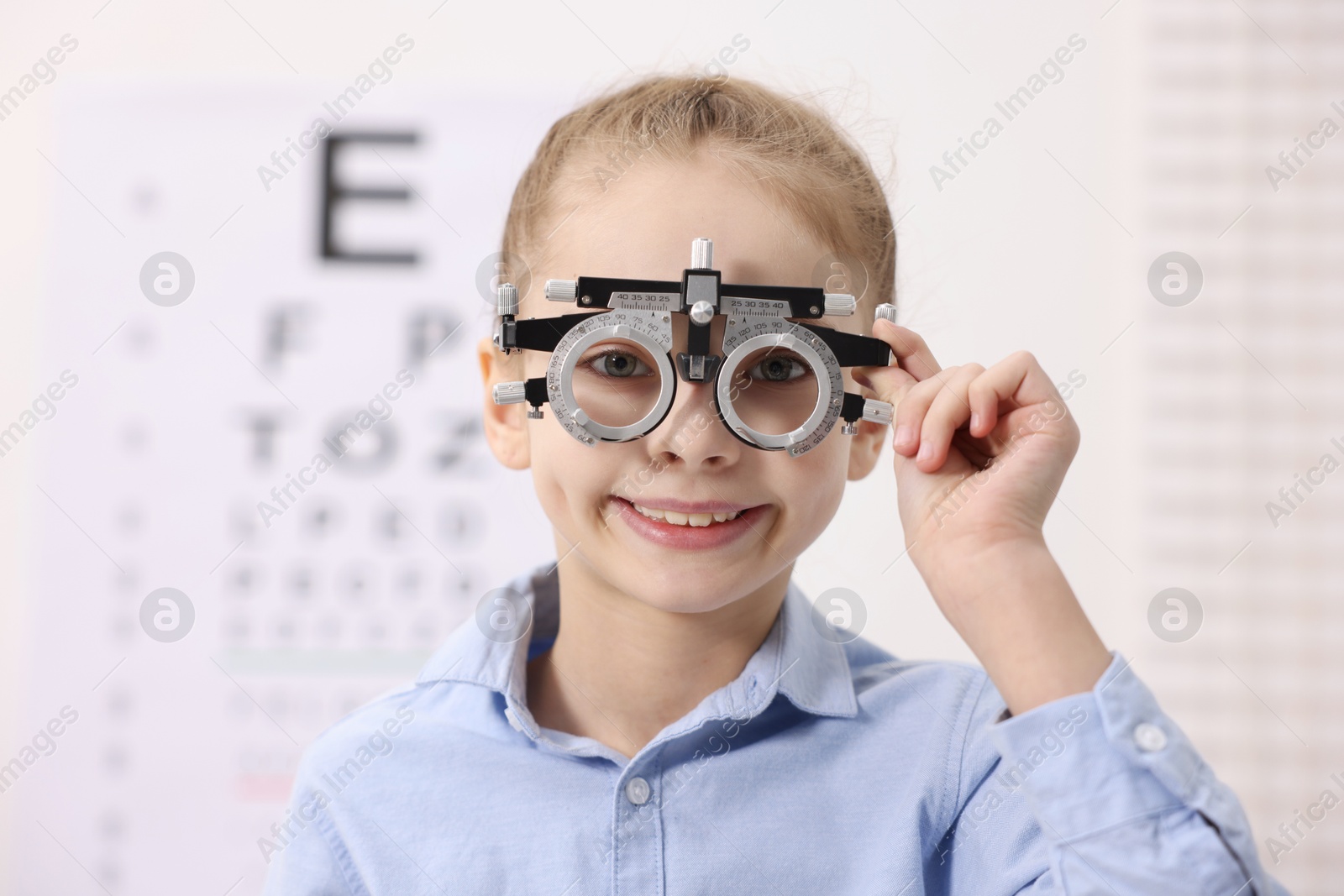 Photo of Little girl with trial frame near vision test chart at ophthalmologist office