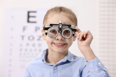 Little girl with trial frame near vision test chart at ophthalmologist office