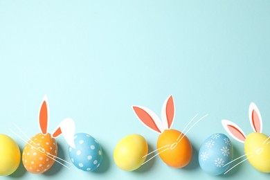 Image of Bright Easter eggs on light blue background, top view. Some of them with bunny ears, noses and whiskers