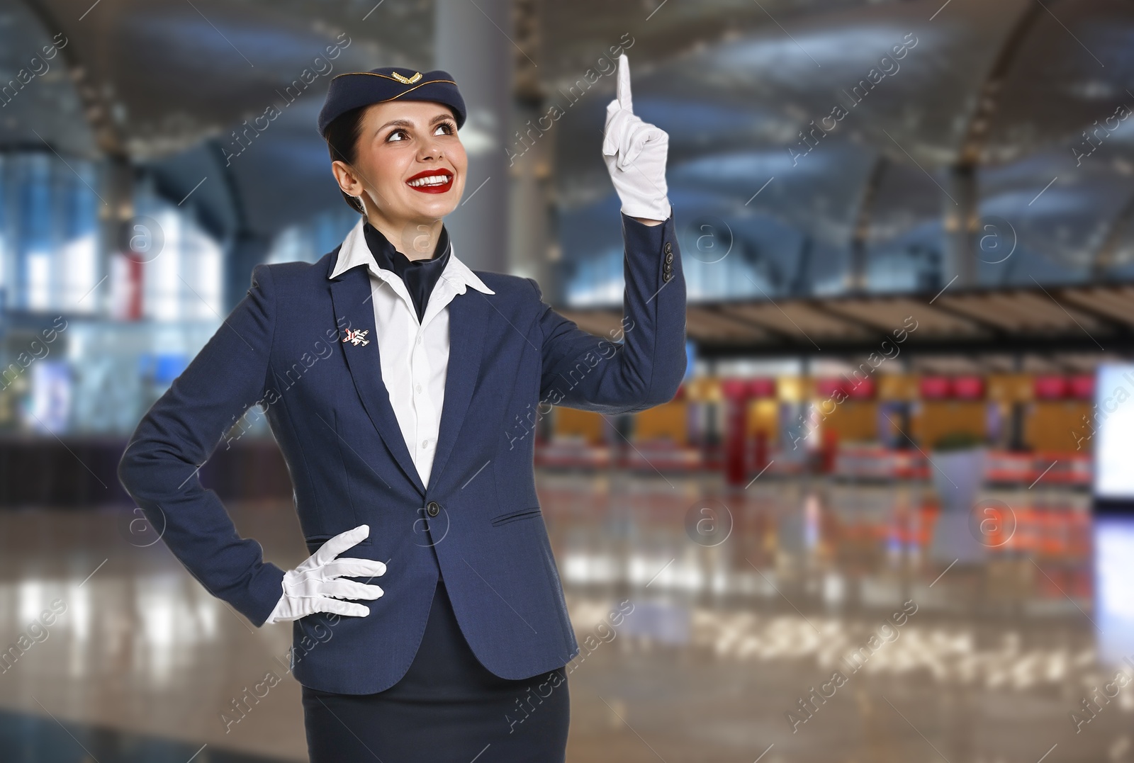 Image of Smiling stewardess pointing upwards in airport terminal. Space for text