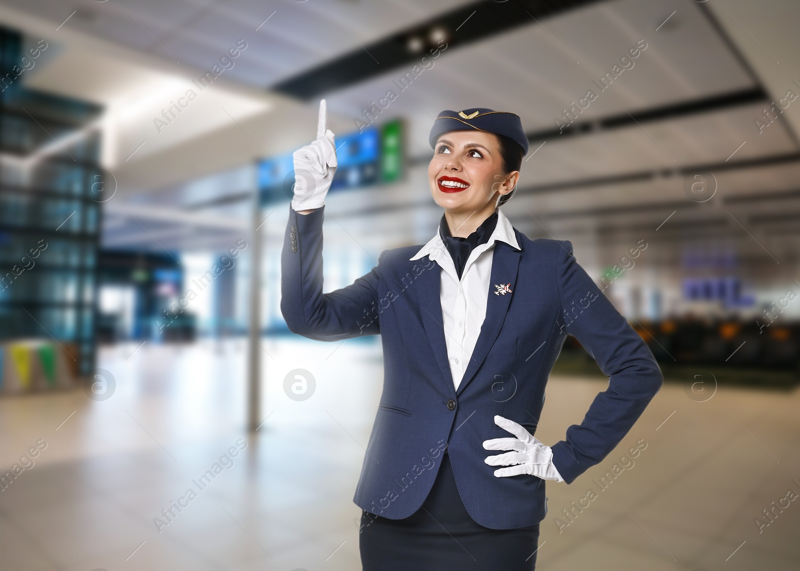 Image of Smiling stewardess pointing upwards in airport terminal. Space for text