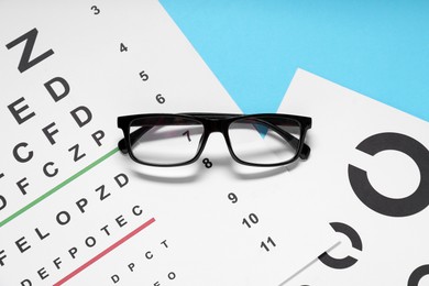 Photo of Glasses and vision test charts on light blue background, top view