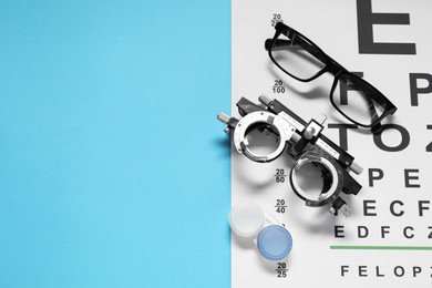 Photo of Glasses, trial frame, vision test chart and lenses on light blue background, flat lay. Space for text