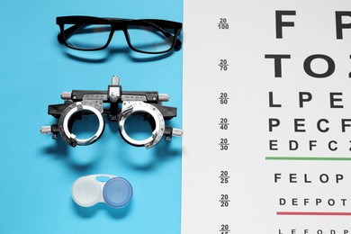 Photo of Glasses, trial frame, vision test chart and lenses on light blue background, flat lay