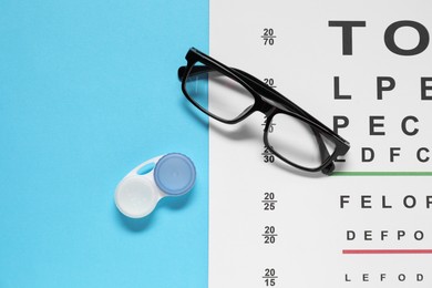 Photo of Glasses, vision test chart and lenses on light blue background, flat lay