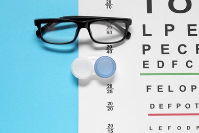 Photo of Glasses, vision test chart and lenses on light blue background, flat lay