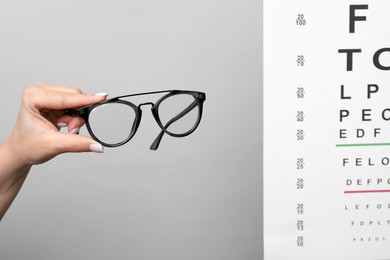 Photo of Woman holding glasses near vision test chart on gray background, closeup