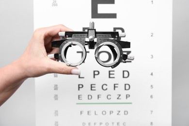 Photo of Woman holding trial frame against vision test chart on gray background, closeup