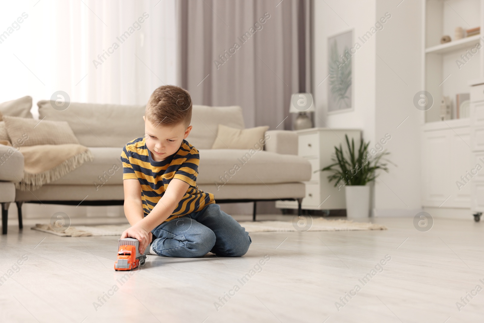 Photo of Little boy playing with toy car at home. Space for text