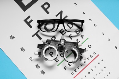 Photo of Glasses, trial frame and vision test chart on light blue background, flat lay