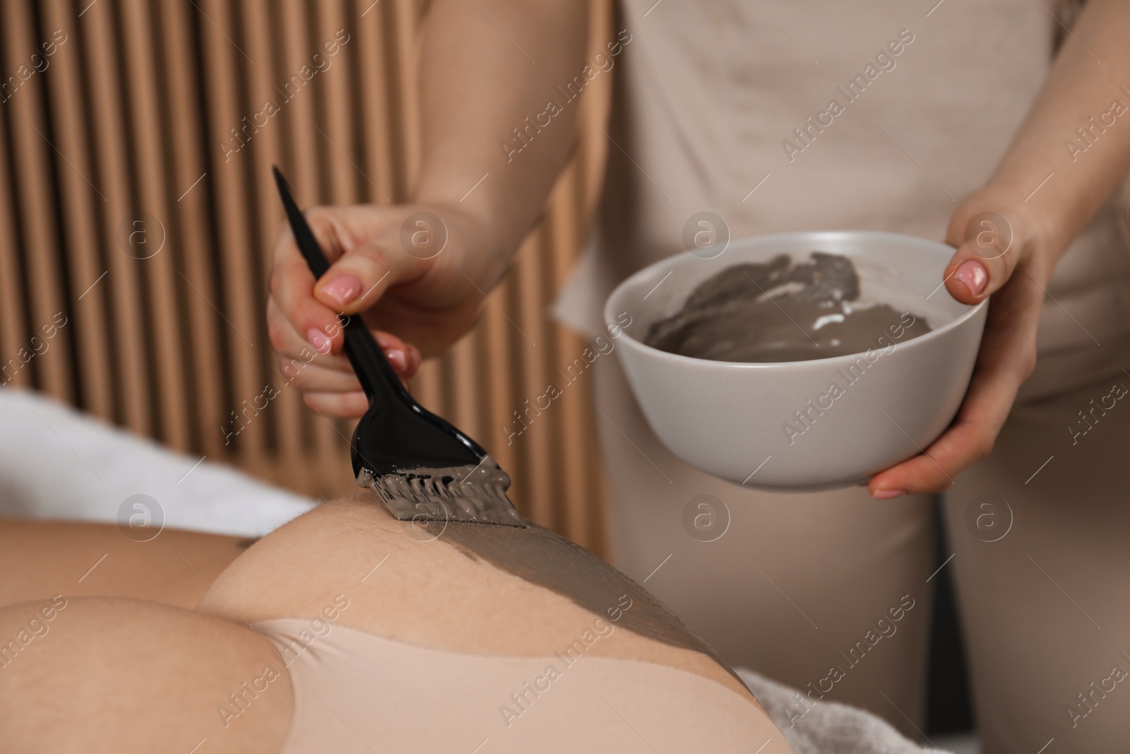 Photo of Esthetician applying cosmetic product for body wraps treatment onto woman's buttocks in spa salon, closeup