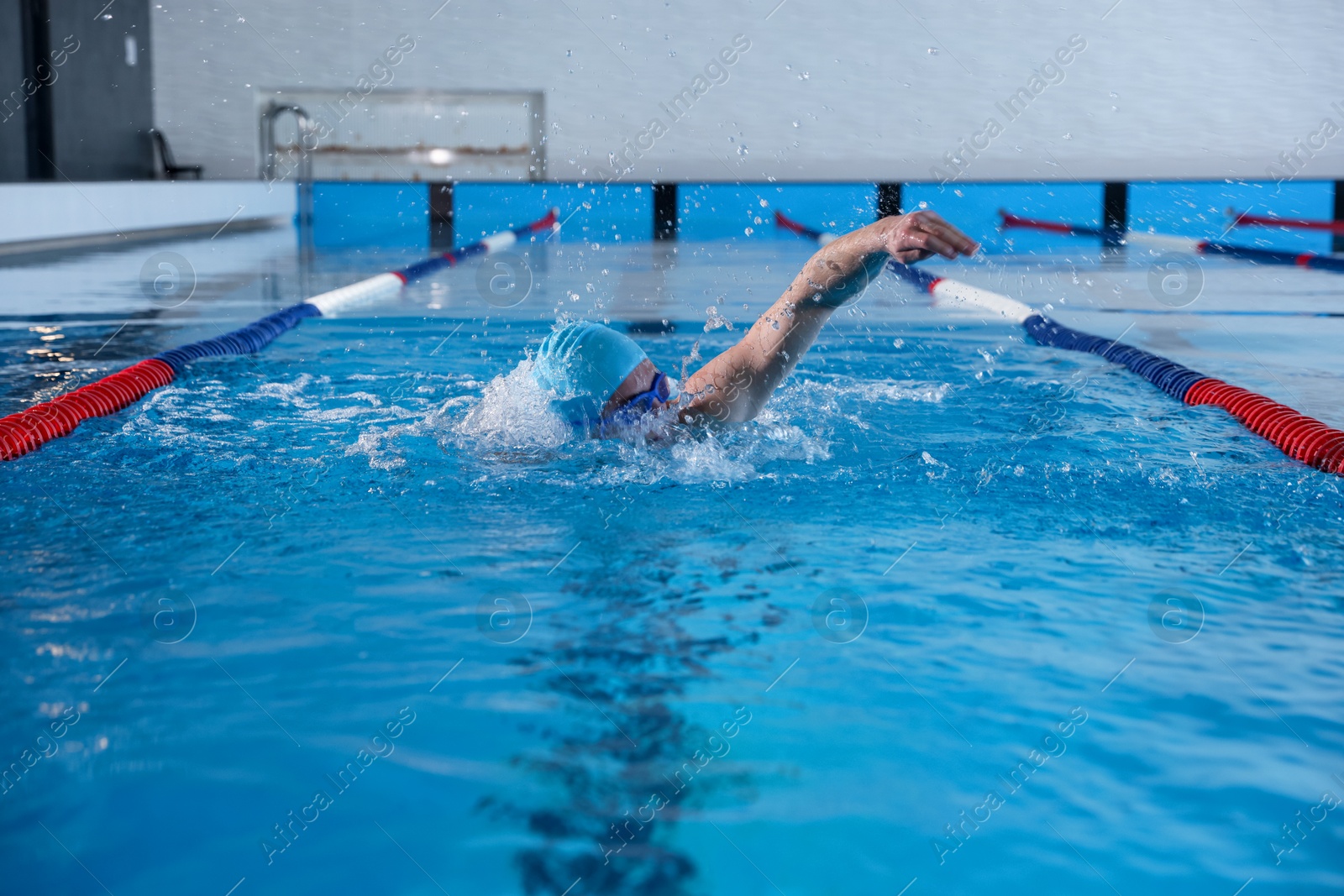 Photo of Young man in cap and goggles swimming in pool indoors