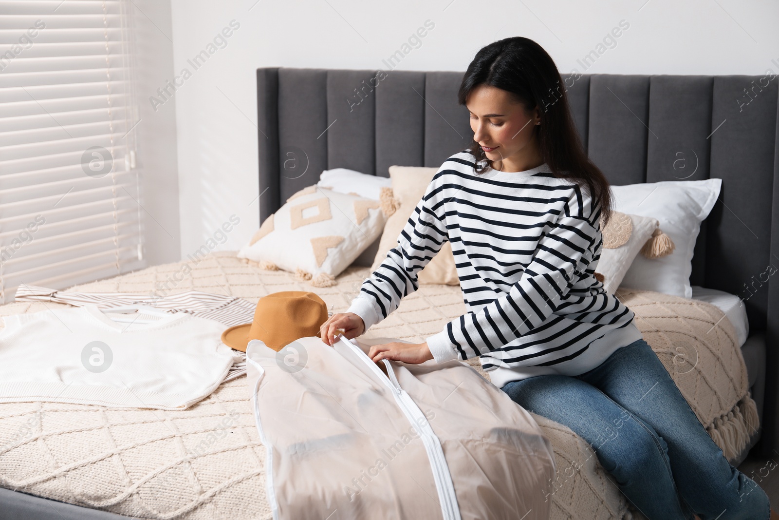 Photo of Woman putting clothes into garment cover on bed indoors