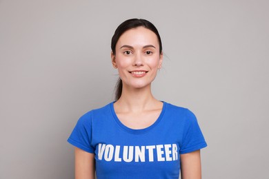 Photo of Young beautiful woman wearing t-shirt with printed word Volunteer on grey background