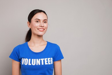 Photo of Young beautiful woman wearing t-shirt with printed word Volunteer on grey background. Space for text