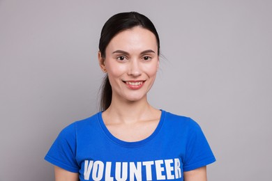 Young beautiful woman wearing t-shirt with printed word Volunteer on grey background