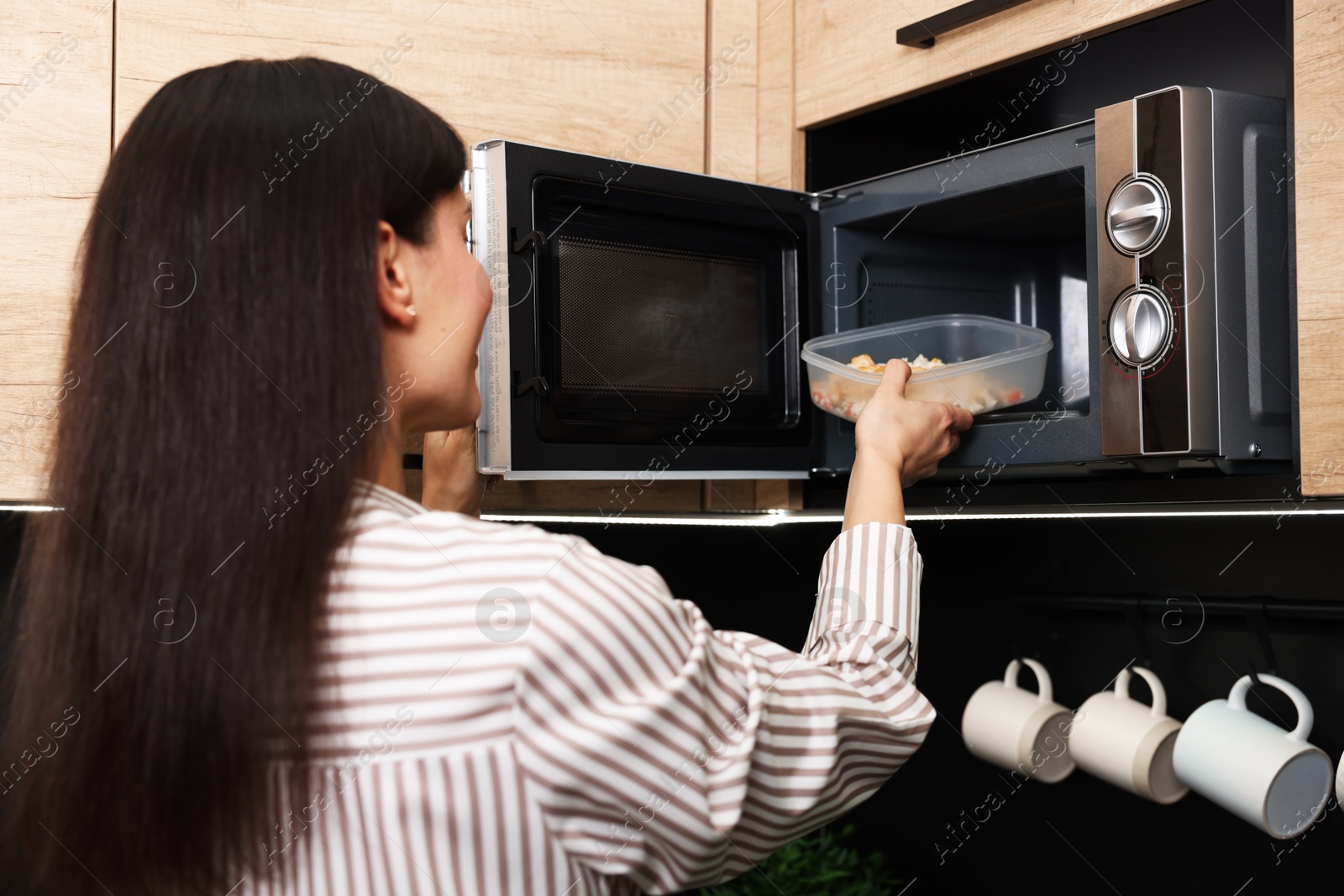 Photo of Woman putting container with lunch into microwave indoors