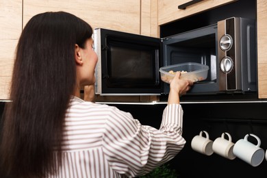 Woman putting container with lunch into microwave indoors