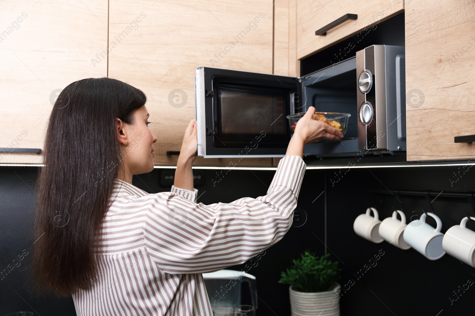 Photo of Woman putting container with lunch into microwave indoors