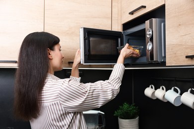 Woman putting container with lunch into microwave indoors