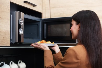 Photo of Woman putting plate with lunch into microwave indoors