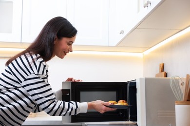 Photo of Woman putting plate with lunch into microwave indoors