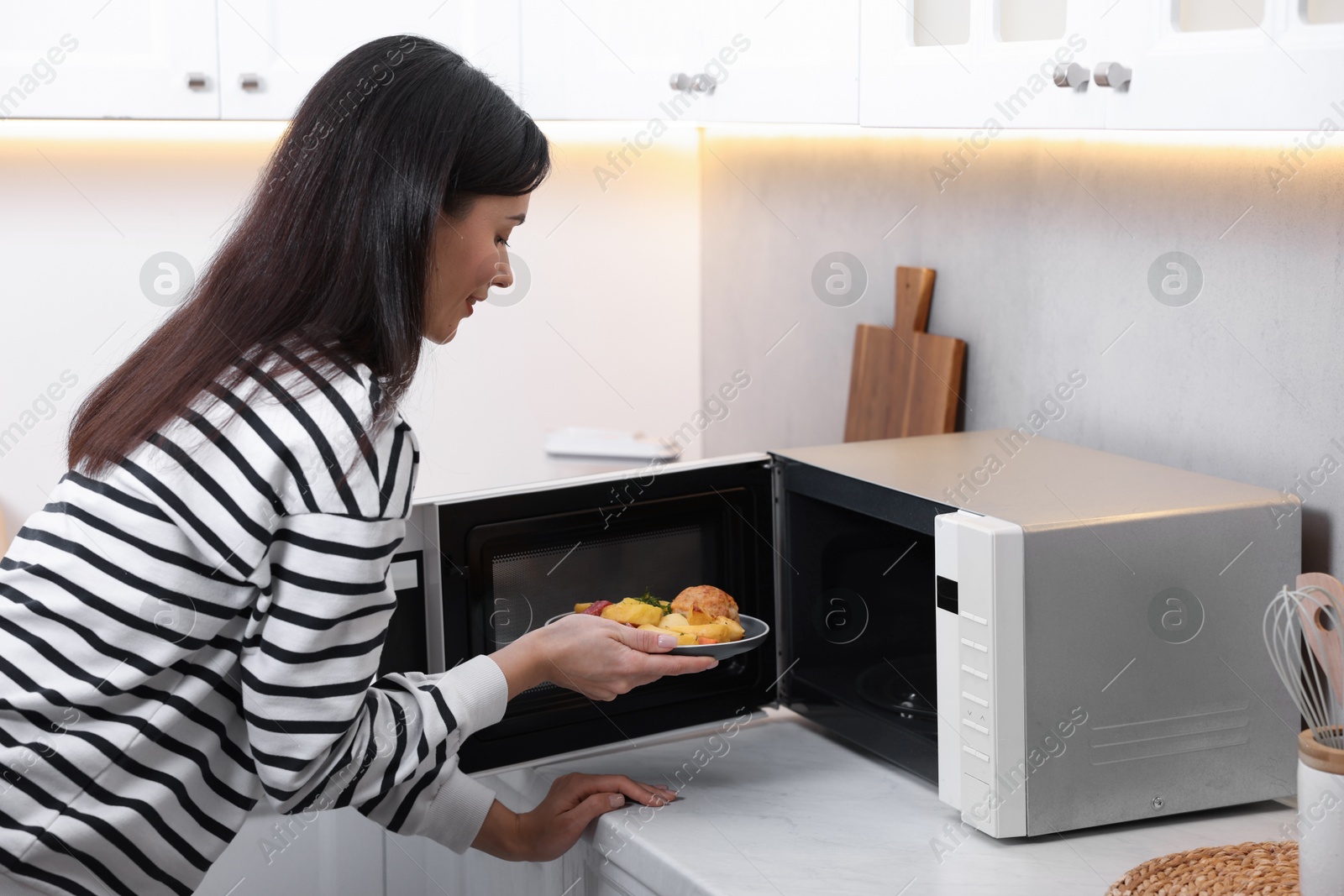 Photo of Woman putting plate with lunch into microwave indoors