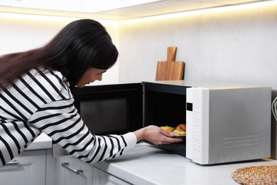 Woman putting plate with lunch into microwave indoors