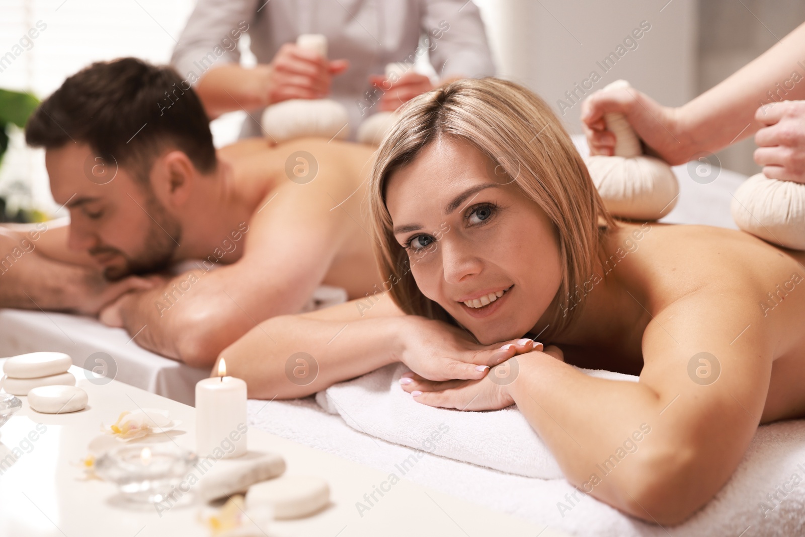 Photo of Happy couple receiving relaxing massage with herbal bags in spa salon, selective focus