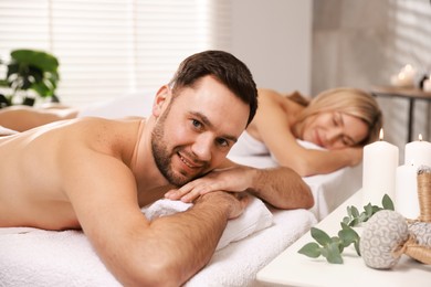 Happy couple lying on massage tables in spa salon, selective focus