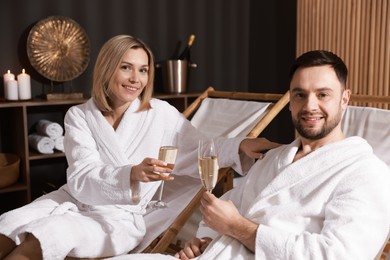 Photo of Happy couple in bathrobes with glasses of champagne relaxing in spa salon