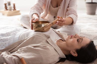 Woman undergoing singing bowl therapy lying on floor indoors