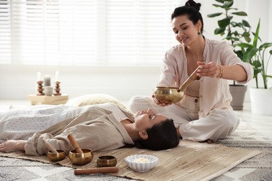 Woman undergoing singing bowl therapy lying on floor indoors. Space for text