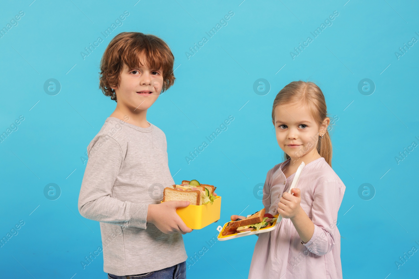 Photo of Cute little children with lunch boxes on light blue background